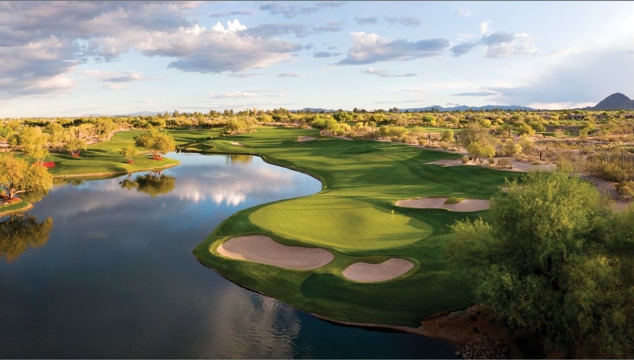 Grayhawk Golf Club lake hole — a peninsula green wrapped in water, with desert landscaping and mountains behind