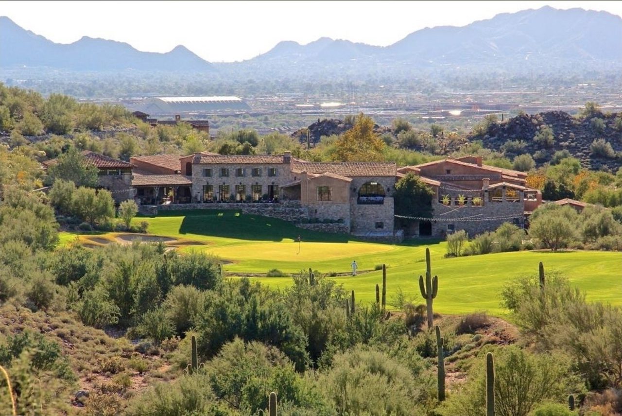 The Silverleaf Club clubhouse seen from the course — stone and stucco buildings with tile roofs above a green, saguaros in the foreground and the Valley behind