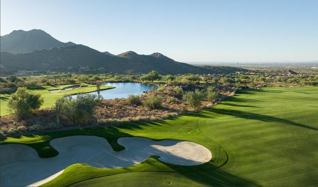 Elevated view over the Silverleaf Club golf course — striped fairways and a sculpted bunker around the course lake, the McDowell Mountains behind